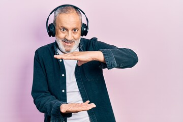 Canvas Print - Handsome senior man with beard listening to music using headphones gesturing with hands showing big and large size sign, measure symbol. smiling looking at the camera. measuring concept.