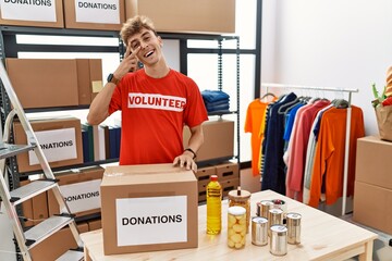 Sticker - Young caucasian man volunteer holding donations box doing peace symbol with fingers over face, smiling cheerful showing victory