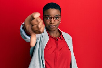 Sticker - Young african american woman wearing business jacket and glasses looking unhappy and angry showing rejection and negative with thumbs down gesture. bad expression.