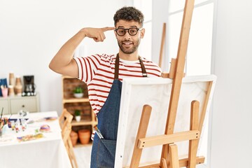 Poster - Arab young man at art studio smiling pointing to head with one finger, great idea or thought, good memory