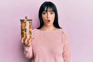 Sticker - Young hispanic woman holding jar with uncooked pasta scared and amazed with open mouth for surprise, disbelief face