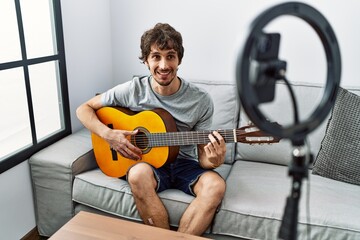 Wall Mural - Young hispanic man having online concert playing classical guitar at home