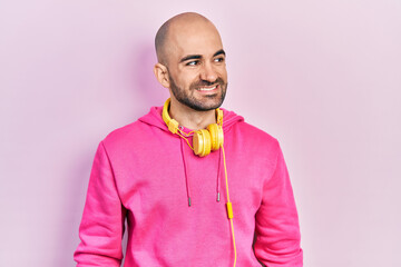 Canvas Print - Young bald man wearing gym clothes and using headphones looking away to side with smile on face, natural expression. laughing confident.