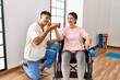 Young disabled woman sitting on wheelchair making mobility exercise using dumbbells at the clinic.