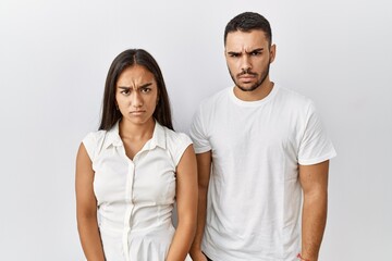 Sticker - Young interracial couple standing together in love over isolated background skeptic and nervous, frowning upset because of problem. negative person.