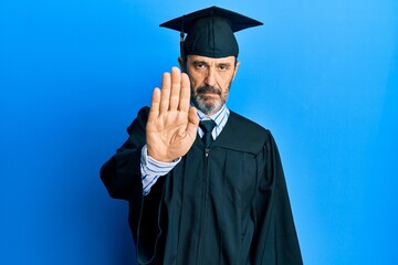 Poster - Middle age hispanic man wearing graduation cap and ceremony robe doing stop sing with palm of the hand. warning expression with negative and serious gesture on the face.