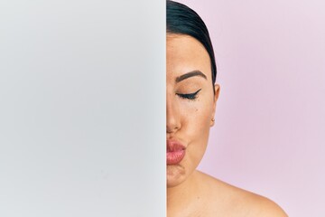 Poster - Beautiful brunette woman holding blank empty banner covering half face looking at the camera blowing a kiss being lovely and sexy. love expression.