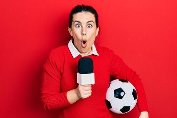 Sticker - Young hispanic woman holding reporter microphone and soccer ball afraid and shocked with surprise and amazed expression, fear and excited face.