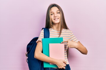 Sticker - Young brunette girl holding student backpack and books smiling happy pointing with hand and finger