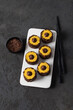 Sweet creamy pumpkin sushi rolls with chocolate sprinkles and filling on a ceramic plate on a dark background top view