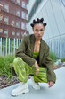 © wayhome.studio - Photo of stylish serious teenage girl dressed in green formal jacket loose trousers and white boots poses against urban buildings outdoors. Fashionable teenager wears stylish outfit in publicity area