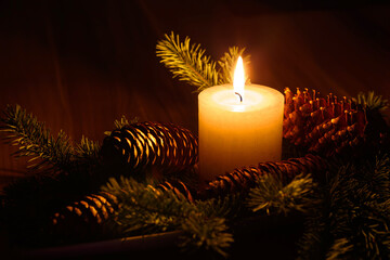 Poster - Closeup of a lit candle, surrounded by pine cones in a dark Christmas setting