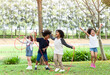 © amorn - Group of diversity kids playing cheerful in the park. Children having fun and jumping with rope in the garden.