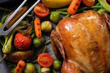 Festive dinner for two of chicken and vegetables. baking sheet with baked chicken and baked green beans, baby carrots, potatoes, green peppers and Brussels sprouts. two glasses of wine.