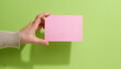 © nndanko - Female hand holding empty pink paper on a green background. Copy paste image or text, close up