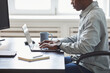 © Seventyfour - Minimal side view shot of young African-American man using laptop while sitting at desk in office, focus on hands typing at keyboard, software developer concept with copy space