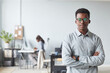 © Seventyfour - Waist up portrait of successful African-American man looking at camera while standing with arms crossed in office, copy space