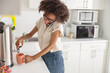 © Yaroslav Astakhov - Smiling Afro American woman preparing hot drink while talking on smartphone on office kitchen