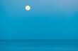 Full moon over the sea against the background of the blue sky