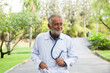 © amorn - Smiling male doctor with stethoscope wear white uniform standing in the park