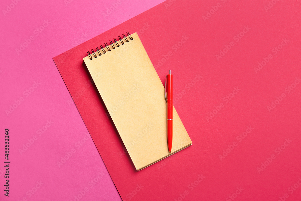 Blank notebook and red pen on color background