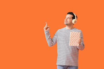 Wall Mural - Young man with book and headphones pointing at something on color background