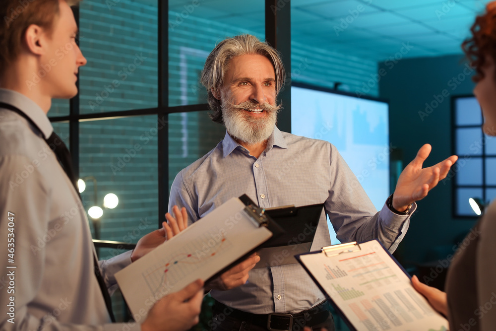 Mature businessman with colleagues working in office at night