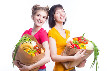 Couple of Positive Caucasian Girls Posing With Eco Paper Bags Filled With Grocery And Vegetables Over Plain Background.