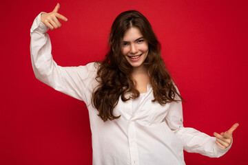 Portrait of beautiful positive cheerful cute smiling young brunette woman in casual white shirt isolated on red background with copy space