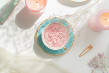 Pink Flower Tea In Vintage Porcelain Tea Cup, Candles, Flowers And Notebook On White Table With Natural Light. Romantic Morning Routine With Healthy Warm Drink. Top View.