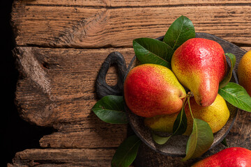 Wall Mural - Fresh ripe pears with green leaves in a bowl on rustic wooden background. Top view with copy space