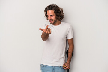 Young caucasian man with crutches isolated on gray background pointing with finger at you as if inviting come closer.