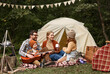 © JenkoAtaman - Father, mother and little son sitting near tourist tent and playing guitar during camping
