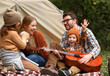 © JenkoAtaman - Father, mother and little son sitting near tourist tent and playing guitar during camping