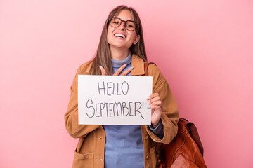 Wall Mural - Young caucasian student woman holding hello September placard isolated on pink background laughs out loudly keeping hand on chest.