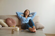 © Evrymmnt - Kick back and relax concept. Young beautiful brunette woman with blissful facial expression alone on the couch with her bare feet on coffee table. Portrait of relaxed female resting at home.