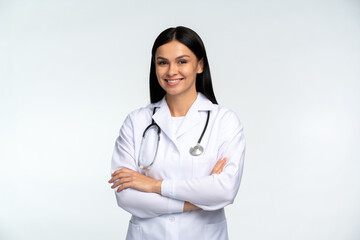 Wall Mural - Portrait of beautiful young female doctor in white medical jacket isolated on white background. Brunette woman medic crossed hands and smiling at the camera