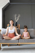 © Вадим Каштанов - Young mother with her little daughter sitting in lotus position on couch. Meditation and relaxation home.