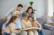 © Studio Romantic - Happy big family grandparents with twin granddaughters and their parents browse the family photo album and share happy memories. Family gathered together in the living room. Family connection concept.