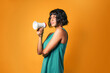 Pretty European woman wearing a teal tank top talking loud on a megaphone against an orange background