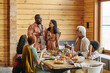 © pressmaster - African young couple holding glasses with wine and saying the toast for their family at the table