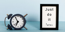 Overturned Alarm Clock And Frame With Words: Just Do It Later. Laziness, Slow Life And Procrastination Concept.