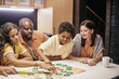 © pressmaster - Happy parents sitting at the table and playing with children in board game at home