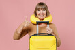 © ViDi Studio - Traveler tourist mature elderly senior lady woman 55 years old wear brown shirt neck pillow hold suitcase bag show thumb up like gesture isolated on plain pastel light pink background studio portrait