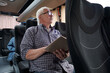 © pressmaster - Mature man with open book looking through window while sitting in bus and traveling between cities