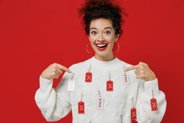 Young smiling surprised fun happy female costumer woman 20s wear white knitted sweater with tags sale in store showroom point index fingre on herself isolated on plain red background studio portrait.