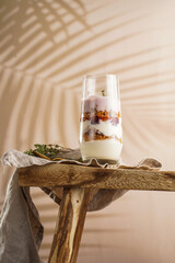 Wall Mural - Tall glass with a layered creamy yoghurt dessert trifle with cookies, amaretti, cherries and thyme on a linen cloth on a rustic wooden table at a tropical setting