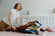 © Sergey Narevskih/Stocksy - Woman throwing stack of clothes on bed