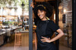 © BONNINSTUDIO/Stocksy - Smiling black waitress standing near entrance of cafe