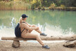 © Evgeniya Grande - Back view faceless portrait of caucasian woman 30-35 years old with backpack in beige sportswear sitting on a log and looking at a mountain lake, walking in the fall woods on vacations.